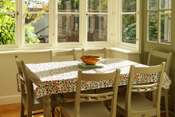 Sunny dining room with floral tablecloth and natural light bringing warmth to interior. Cotswolds countryside, England