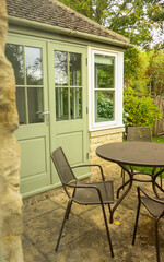 Cozy patio setting with garden furniture, green doors, and stone wall. Cotswolds countryside, England