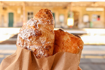 Almond croissant and pain au chocolat in paper bags, ready for a travel breakfast snack at a train...
