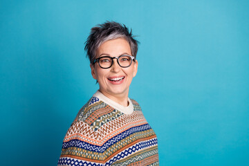 Stylish senior woman with short gray hair and glasses laughing cheerfully against a vibrant blue...