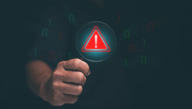 Cybersecurity warning concept. Businessman holding magnifying glass and glowing red alert icon. symbolizing data breach detection, system error alert, online threat and digital risk management.