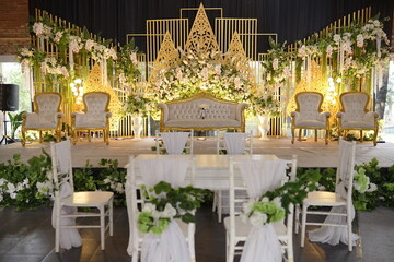 Elegant wedding stage decorated with lush white flowers, gold accents, and seating for guests