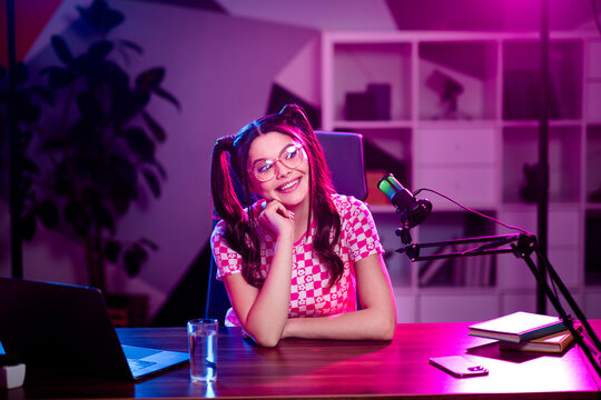 Young female podcaster streaming content from a modern workspace with vibrant neon pink lighting and creative tools