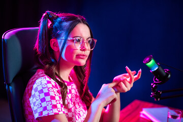 Young female blogger in a pink-themed setup recording a podcast with a professional microphone and neon lighting