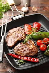 Pan with grilled beef steaks, rosemary, vegetables and carving fork on wooden table, closeup