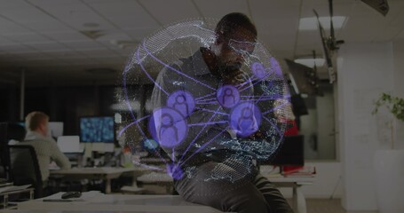 African American man sitting on desk in office, using smartphone and projecting holographic globe