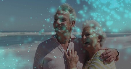 Smiling senior couple embracing on sandy shore gazing at horizon, wearing light shirt, striped top