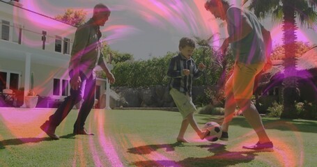 Naklejka premium Kicking soccer ball, father, grandfather and son taking turns on grass lawn, with hedges, palm tree