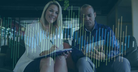 Reviewing overlay on tablet noting on clipboard in office lounge, with chart data and leather sofa