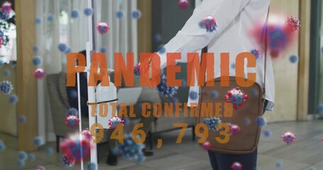 Sanitizing medic using sanitizer dispenser in hall with brown bag, virus and PANDEMIC 946,793 over