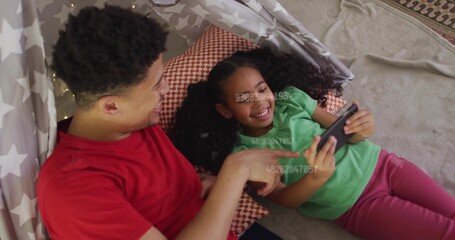 Sharing joy, father and daughter exploring tablet in star-patterned play tent, with string lights