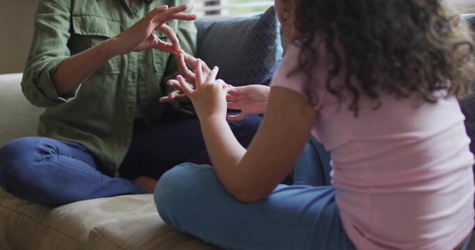 Communicating mother and daughter sitting legs crossed on sofa at home with pillow and blinds