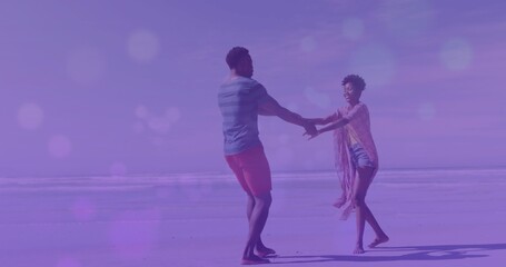 Spinning couple clasping hands wearing beachwear on sandy beach, reflecting sand and ocean horizon