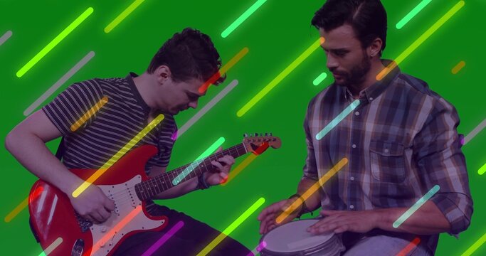 Two bandmates strumming red electric guitar and tapping hand drum in studio, neon streaks