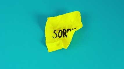Video stop motion of Crumpled yellow note with 'SORRY' handwritten in black ink isolated on blue backgrounds