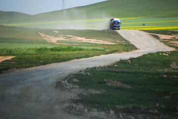 A truck driving on a rural dirt road in a green field