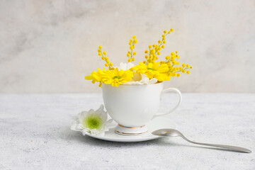 Cup with beautiful flowers, saucer and spoon on light grunge background