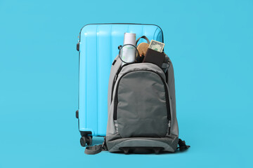 Suitcase, backpack with travelling belongings and magnifying glass on blue background