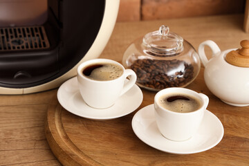 Cups of hot espresso and jar with beans on kitchen countertop