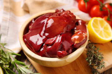 Bowl of raw liver with rosemary, cut lemon and thyme, closeup