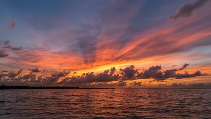 Naklejka premium Vibrant Sunset over Calm Ocean with Coastal Silhouette
