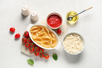Baking dish with raw conchiglie pasta, bowls of tomato sauce, cheese and oil on light background