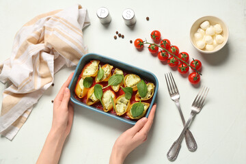 Woman holding baking dish of stuffed conchiglie pasta on light background