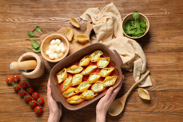 Woman holding baking dish of stuffed conchiglie pasta on wooden background
