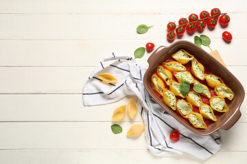 Baking dish of stuffed conchiglie pasta with cheese, spinach and tomato sauce on white wooden background