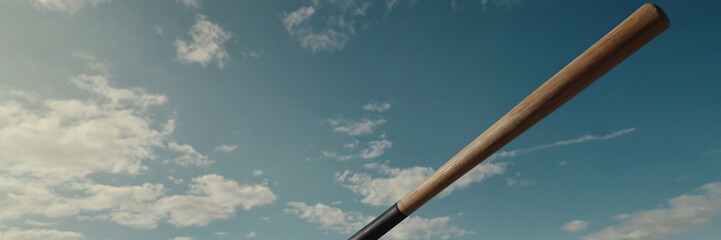 A wooden baseball bat angled upwards against a wide blue sky with soft white clouds