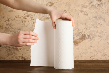 Woman unroll paper towels on wooden table against beige grunge wall