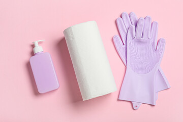 Paper towels with rubber gloves and bottle of soap on pink background
