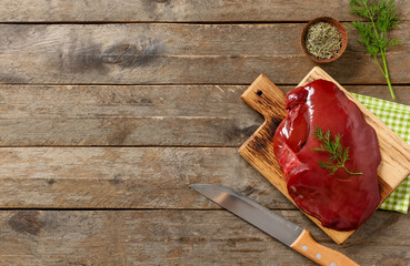 Board with raw liver, dill, bowl of dried rosemary and knife on wooden background