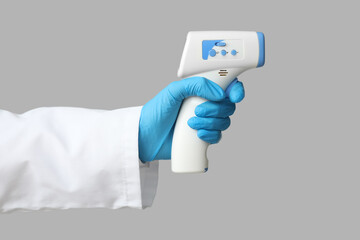 Hand of doctor in rubber glove with infrared thermometer on grey background