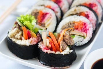 Freshly prepared Gimbap or Kimbap, a popular Korean dish presented on a white plate. This dish is made from rice (bap), beef (bulgogi), radish, lettuce, cucumber, carrot, and wrapped in seaweed.
