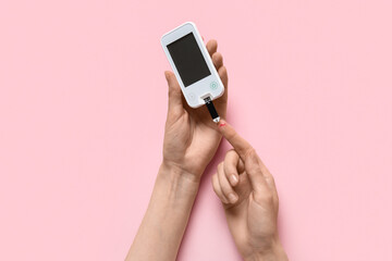 Woman measuring glucose level with digital glucometer on pink background