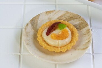 Homemade mini fruit pie dessert topped with cream, orange slice, and jelly on ceramic plate. Perfect for bakery, pastry, and sweet food concepts.