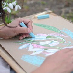 Hands drawing snowdrops with pastel crayons