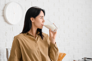 Beautiful young woman drinking milk in kitchen