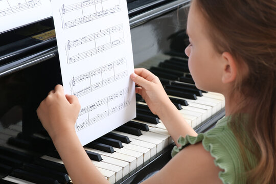 Cute little girl with notes playing grand piano at home