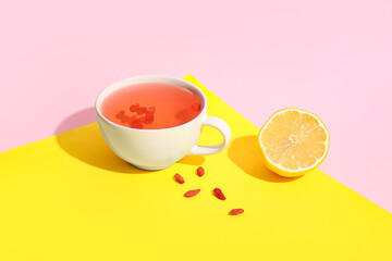 Cup of hot goji tea with lemon and berries on colorful background