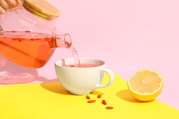 Pouring hot goji tea from teapot into cup on colorful background