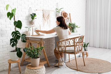 Young woman with notebooks and houseplants at desk in office, back view