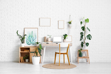 Interior of office with workplace, blank frames and houseplants
