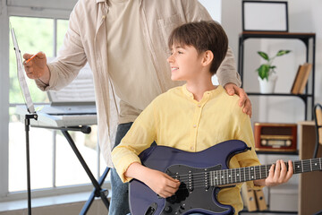 Private music teacher with note sheet giving guitar lessons to boy in room