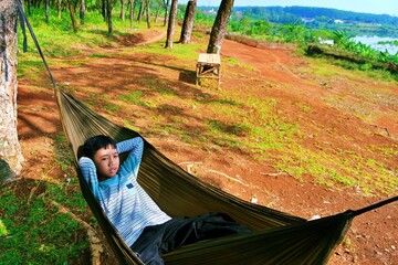 Young Boy lying on hammock with trees and open ground, outdoor lifestyle and relaxation concept.