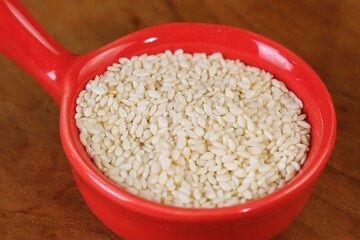 Close up of raw white sesame seeds in red bowl. Healthy ingredient for Asian cooking, bakery, and traditional dishes.