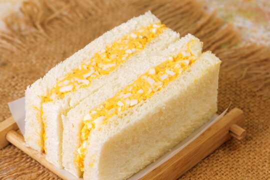 Traditional Japanese egg sandwich Tamago Sando with fluffy bread and creamy egg filling served on wooden plate.