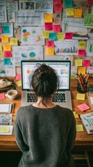 Top view of businesswoman working on laptop while looking at graph and stick sticky notes at whiteboard.  