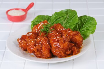Korean yangnyeom chicken served with lettuce garnish and sesame seeds. Crispy fried chicken with spicy sweet sauce.